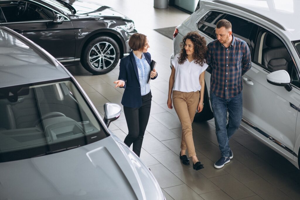 A couple discusses their options with a salesperson while walking through a modern car dealership showroom.