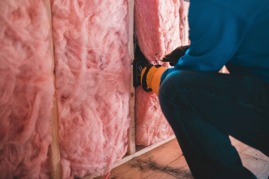 Contractor installing pink fiberglass insulation to improve energy efficiency and fix heat loss in an older home.
